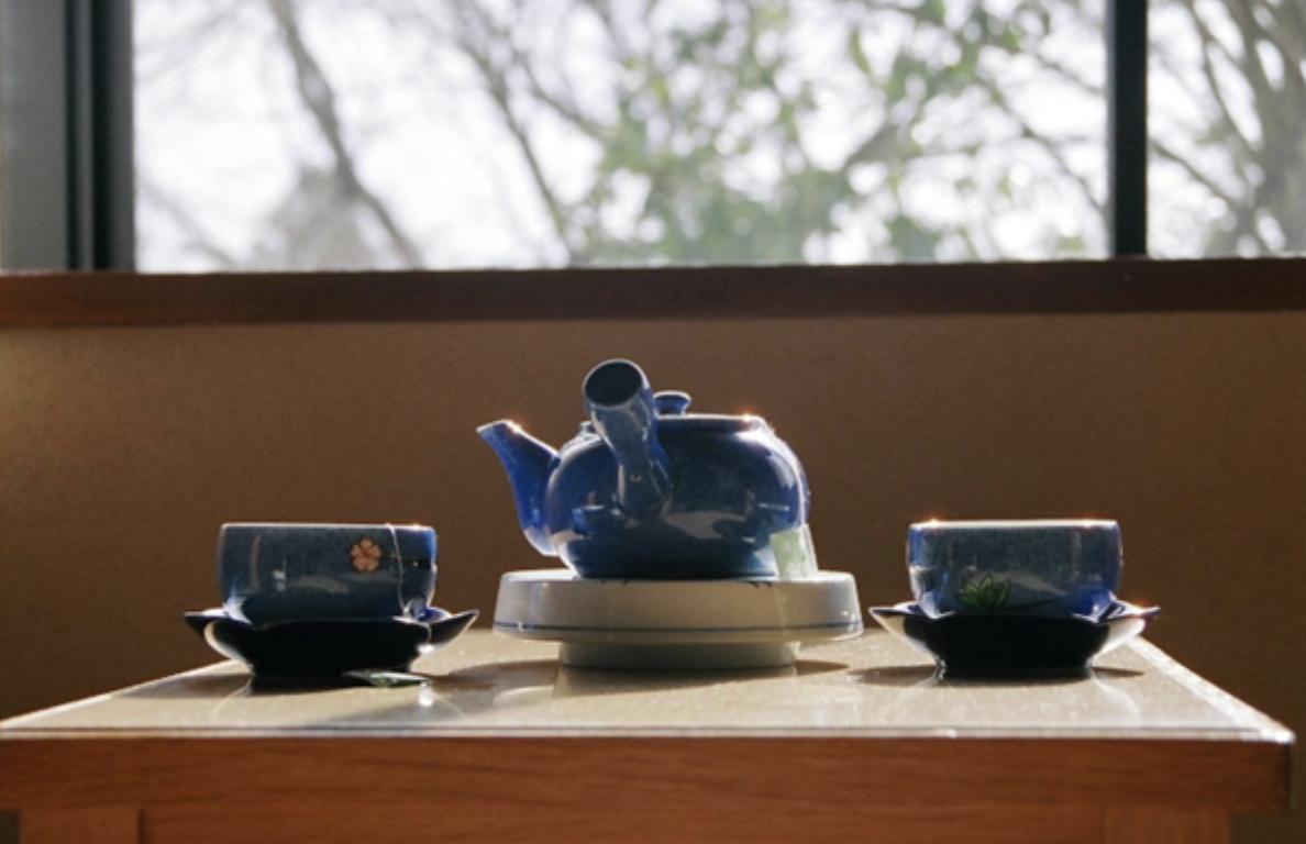 Two cups of tea next to a tea kettle. 